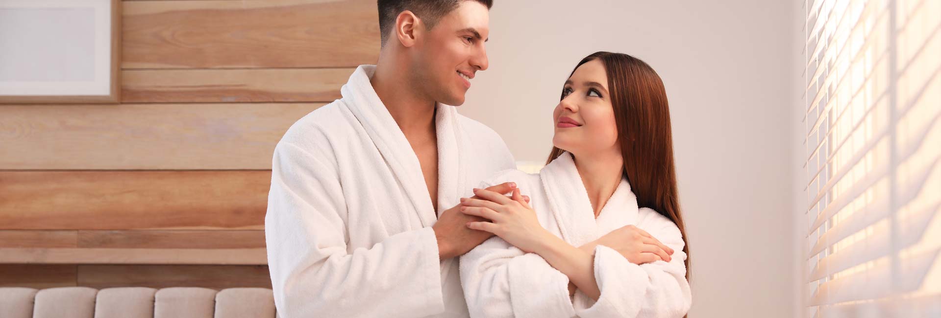 Happy couple wearing bathrobes near window in bedroom